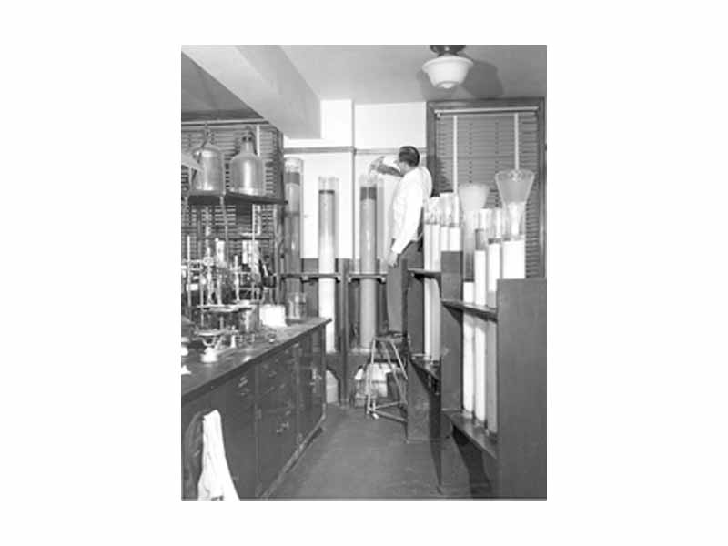 A chemist is shown using column chromatographic apparatus in the mid-1950s to separate constituents in a coal tar color analysis.
